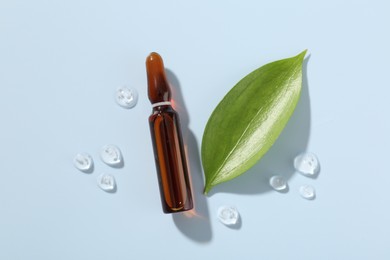 Photo of Glass ampoule with cosmetic product and green leaf on light blue background, flat lay
