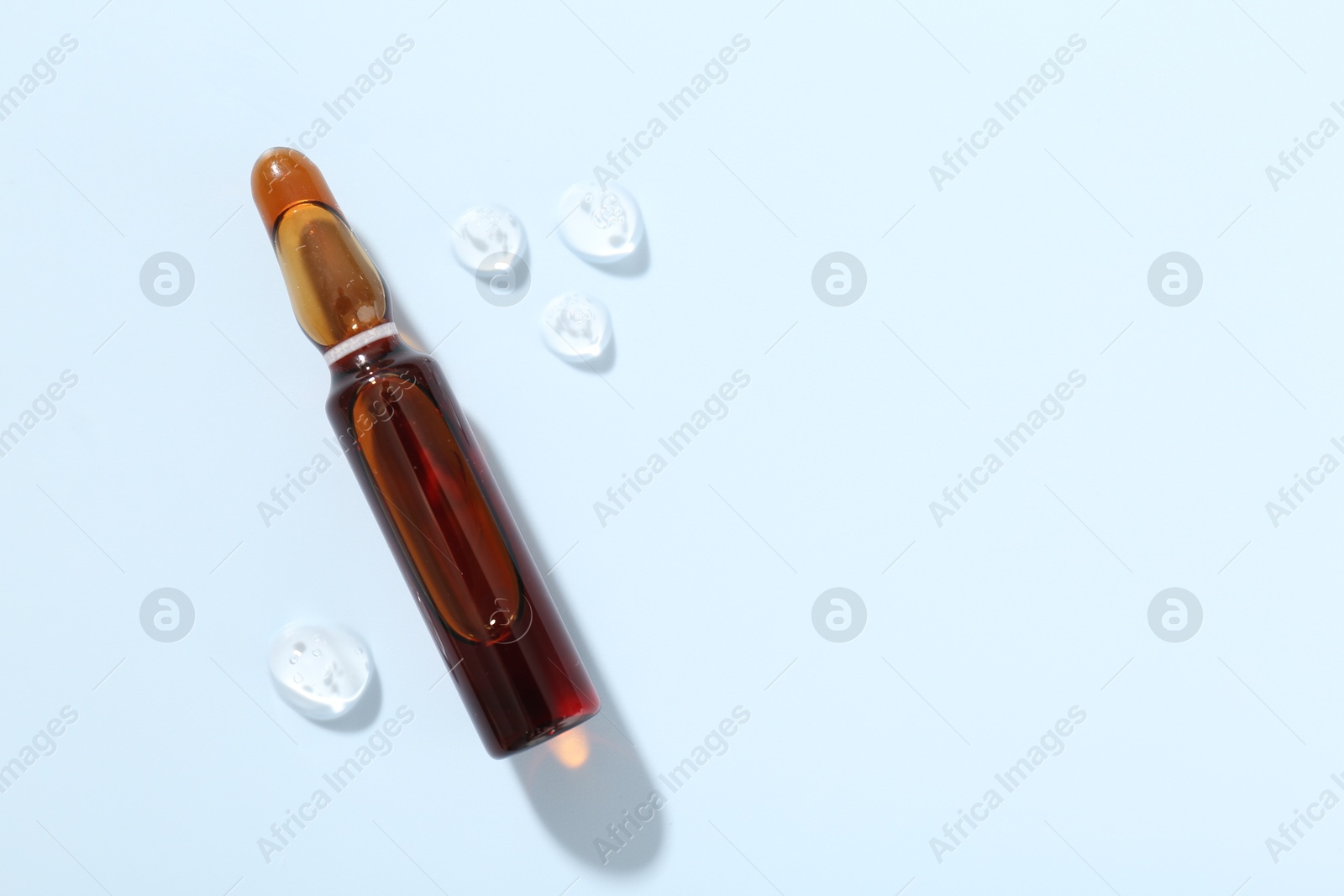 Glass ampoule with cosmetic product on light blue background, top view. Space for text Photo of Glass ampoule with cosmetic product on light blue background, top view. Space for text