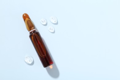 Photo of Glass ampoule with cosmetic product on light blue background, top view. Space for text