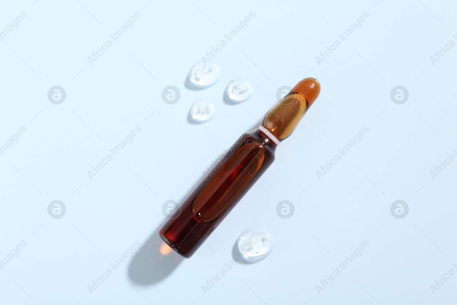 Glass ampoule with cosmetic product on light blue background, top view Photo of Glass ampoule with cosmetic product on light blue background, top view