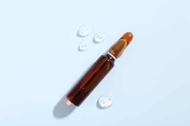 Photo of Glass ampoule with cosmetic product on light blue background, top view