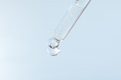 Photo of Dripping cosmetic product from pipette on light blue background, closeup