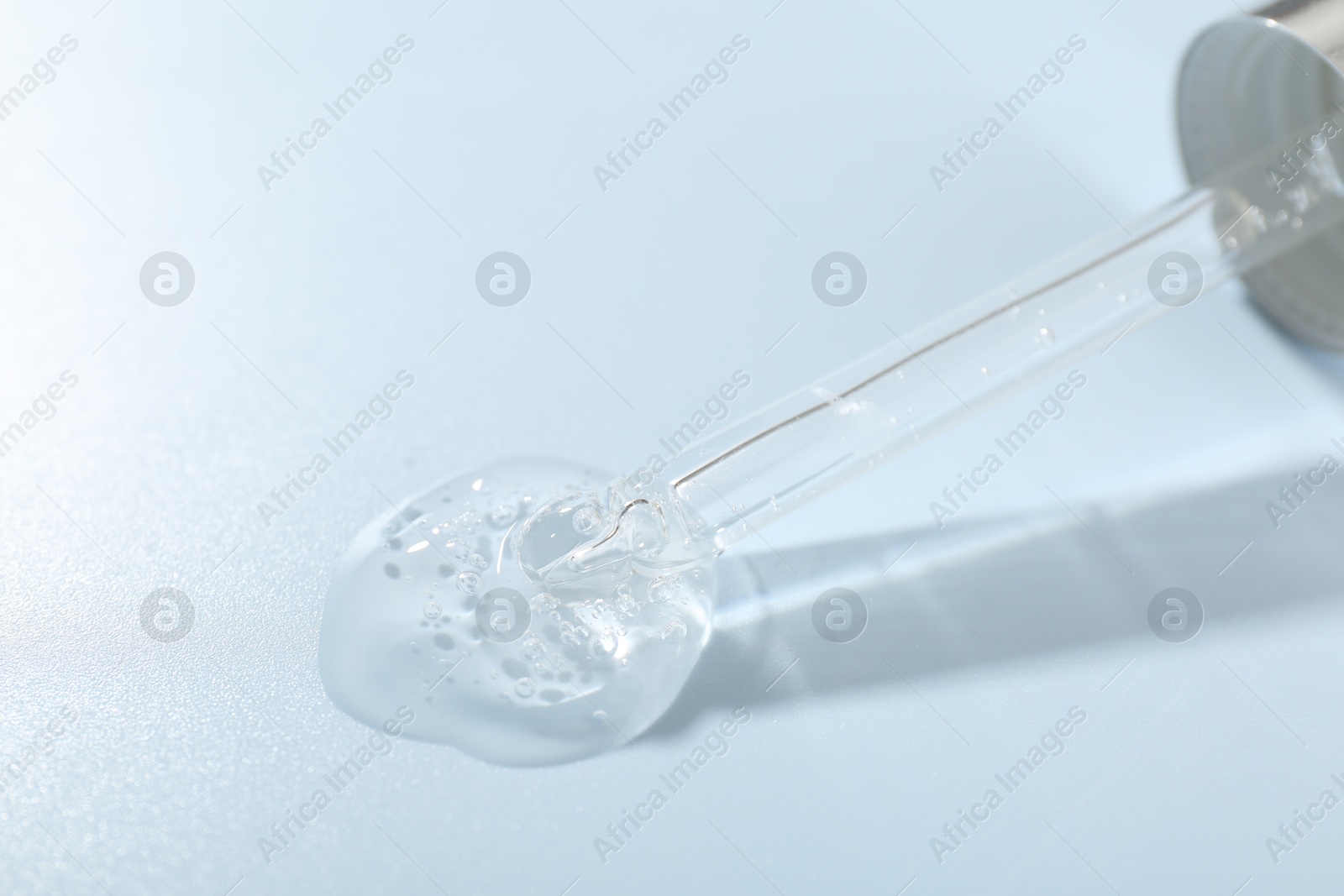 Dripping cosmetic product from pipette on light blue background, closeup Photo of Dripping cosmetic product from pipette on light blue background, closeup