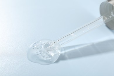 Photo of Dripping cosmetic product from pipette on light blue background, closeup