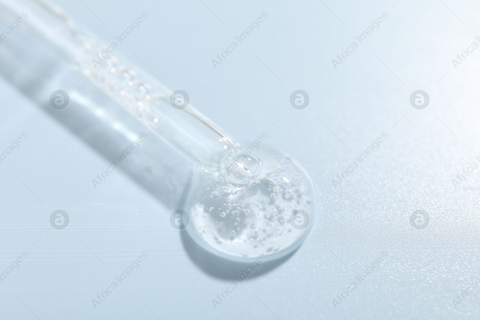 Dripping cosmetic product from pipette on light blue background, closeup Photo of Dripping cosmetic product from pipette on light blue background, closeup