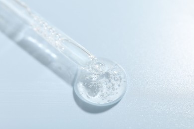 Photo of Dripping cosmetic product from pipette on light blue background, closeup