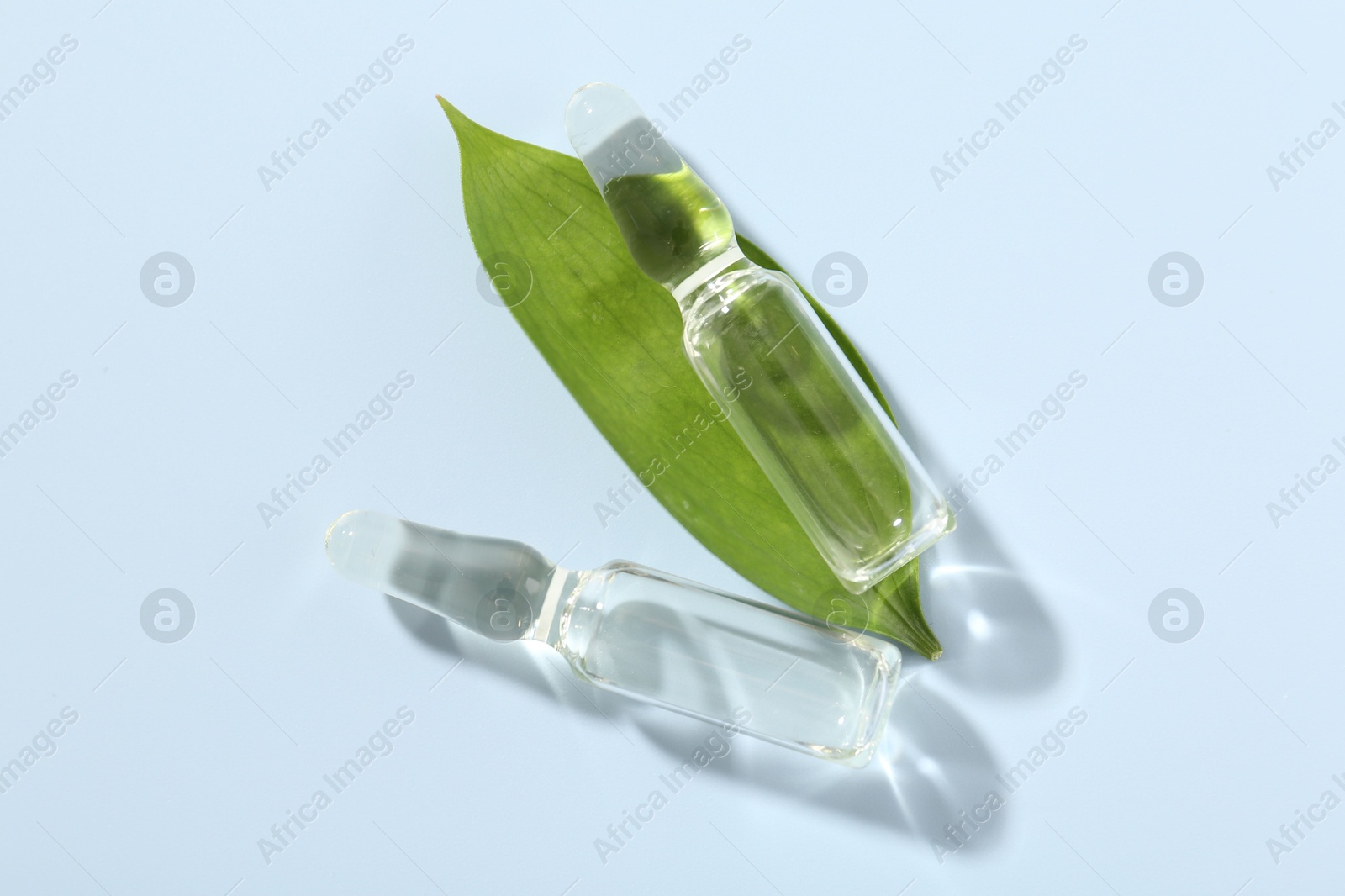 Glass ampoules with cosmetic product and green leaf on light blue background, flat lay Photo of Glass ampoules with cosmetic product and green leaf on light blue background, flat lay