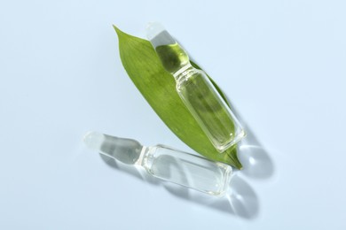Photo of Glass ampoules with cosmetic product and green leaf on light blue background, flat lay