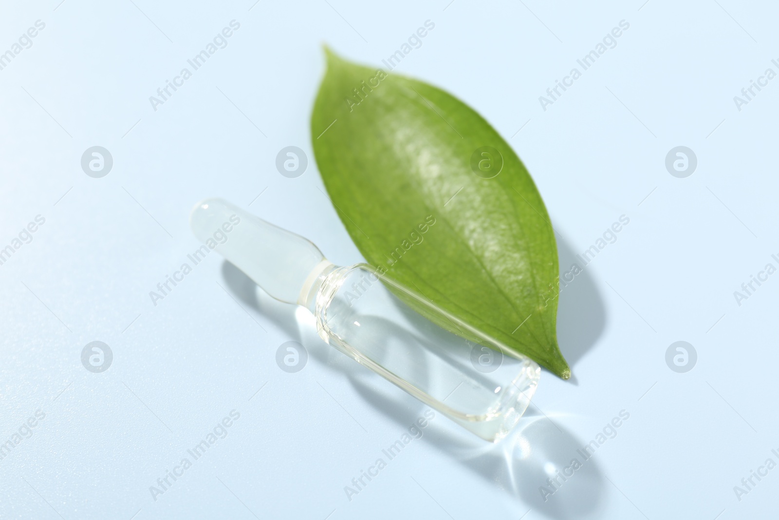 Glass ampoule with cosmetic product and green leaf on light blue background, closeup Photo of Glass ampoule with cosmetic product and green leaf on light blue background, closeup