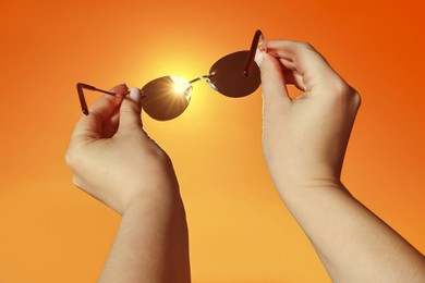 Image of Woman holding sunglasses against orange sky with bright sun, closeup