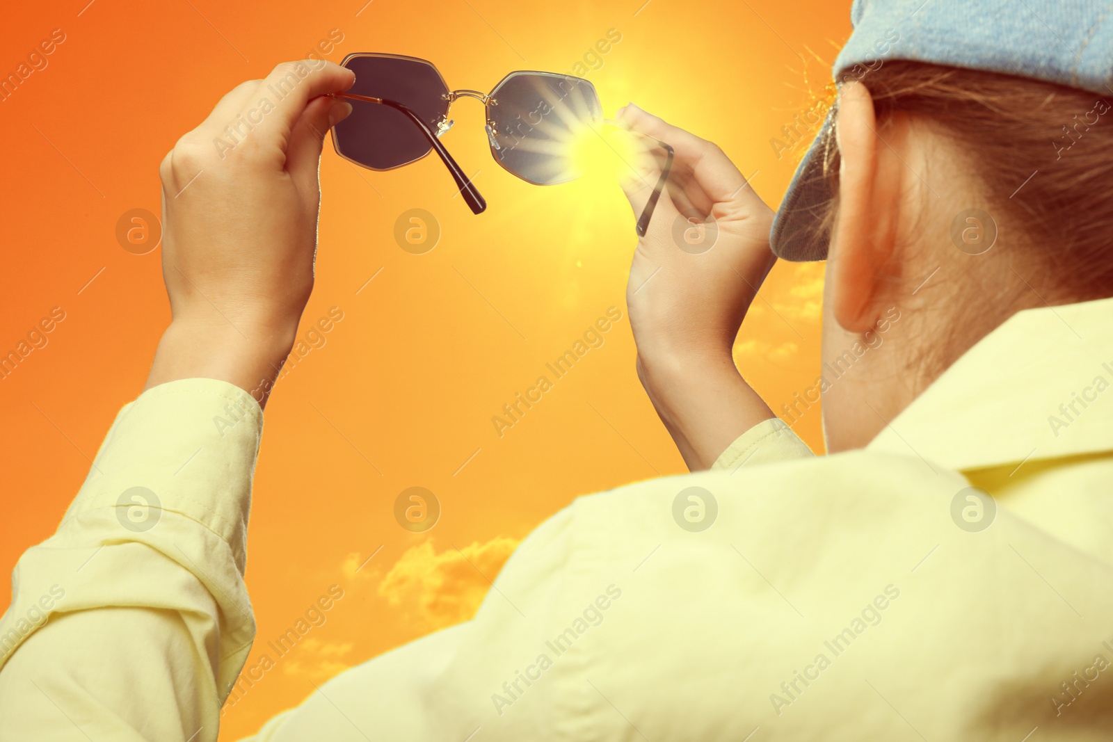 Woman holding sunglasses against orange sky with bright sun, closeup Image of Woman holding sunglasses against orange sky with bright sun, closeup