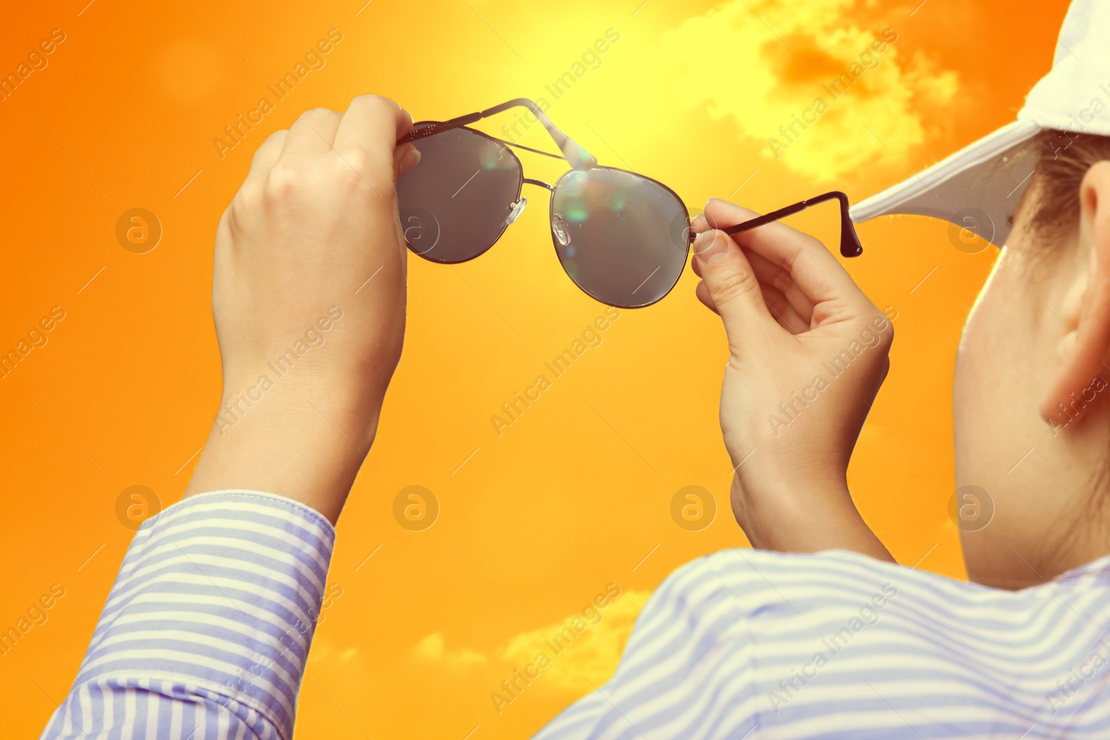 Woman holding sunglasses against orange sky with bright sun, closeup Image of Woman holding sunglasses against orange sky with bright sun, closeup