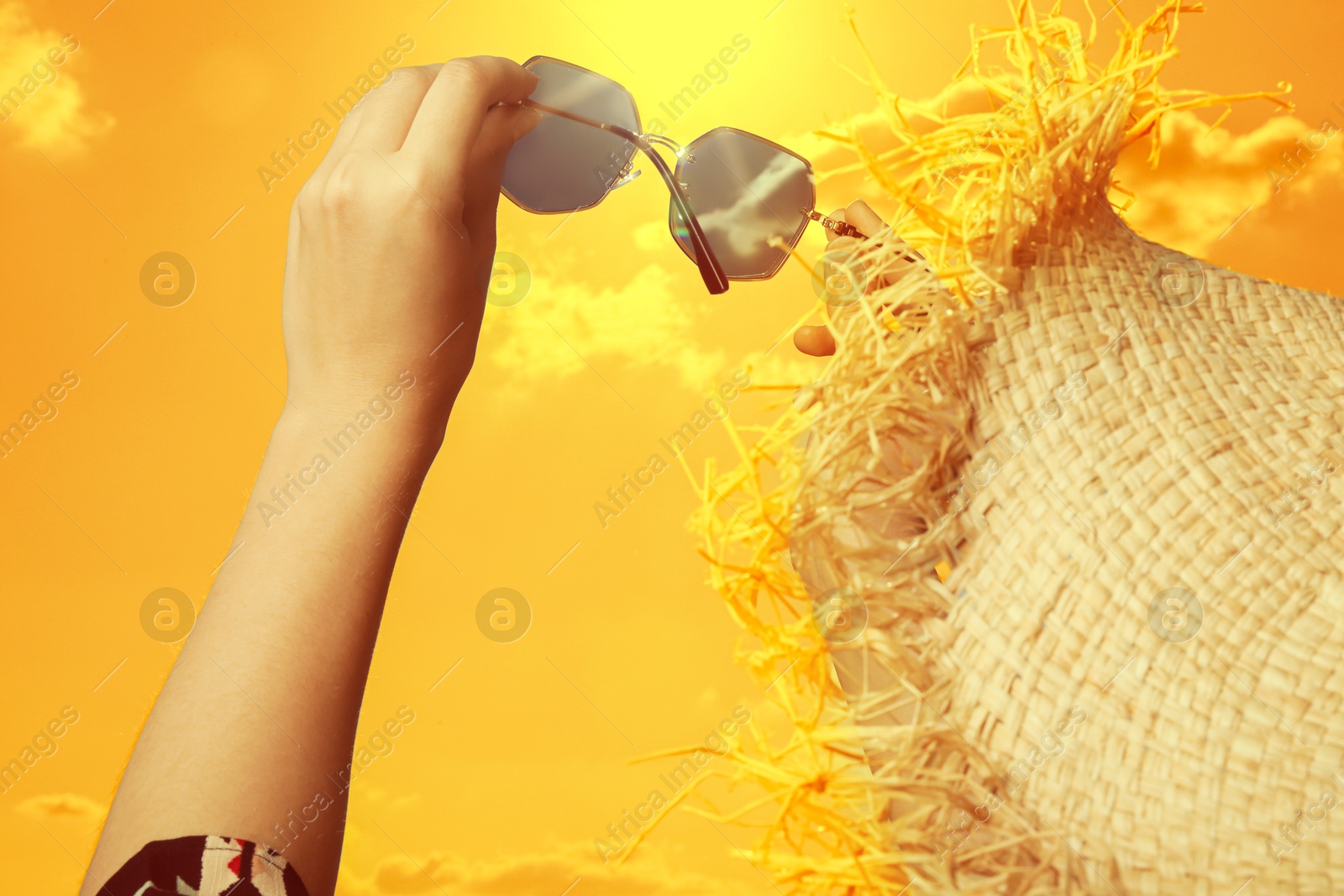 Woman holding sunglasses against orange sky with bright sun, closeup Image of Woman holding sunglasses against orange sky with bright sun, closeup