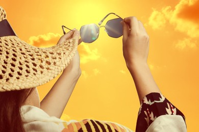 Image of Woman holding sunglasses against orange sky with bright sun, closeup