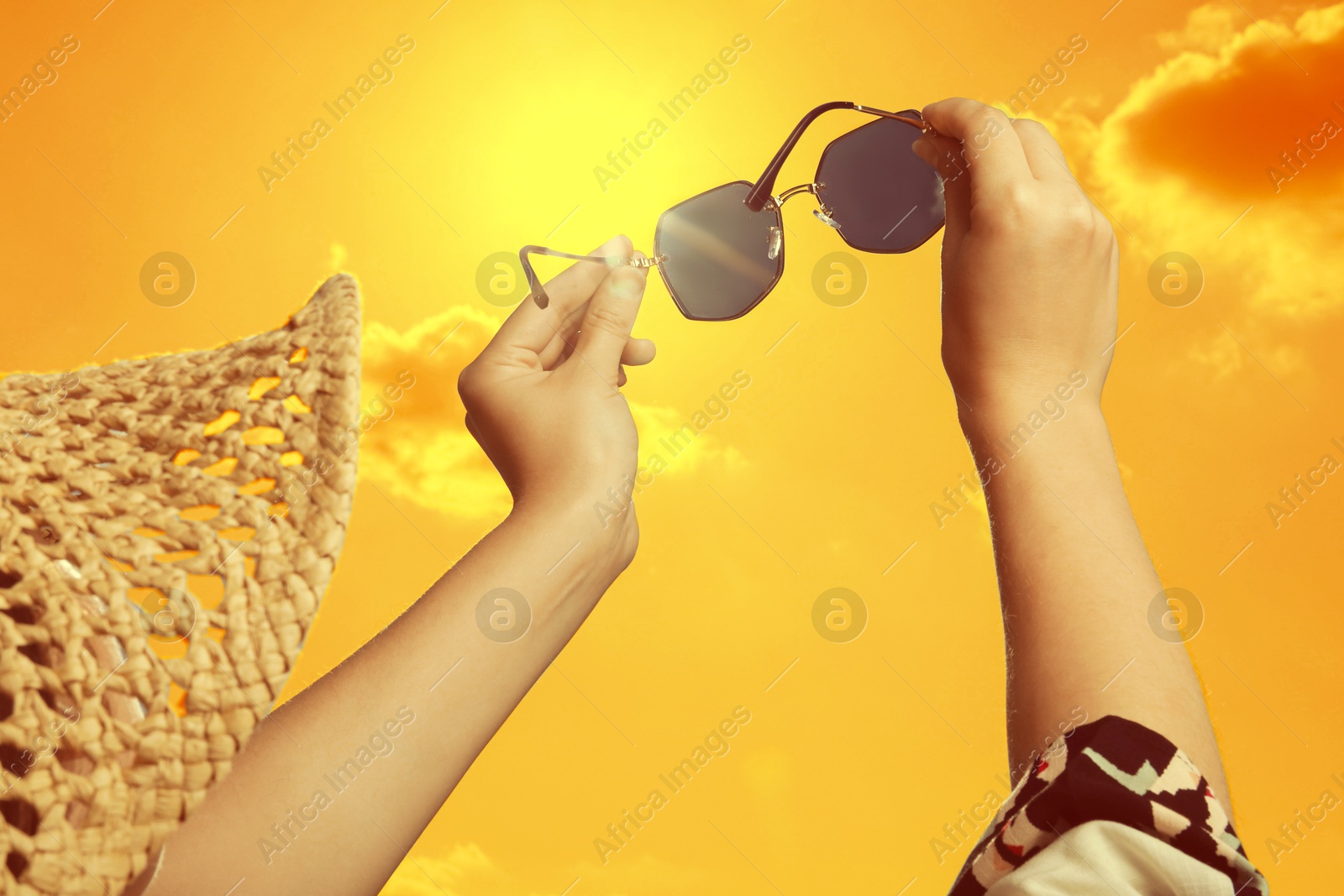 Image of Woman holding sunglasses against orange sky with bright sun, closeup