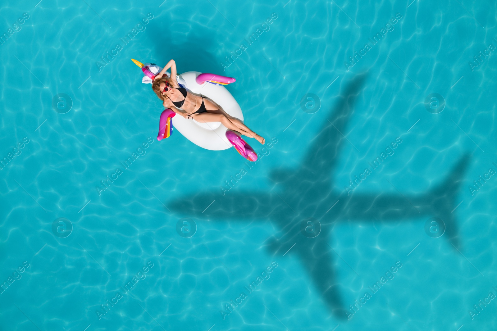 Image of Young happy woman with inflatable ring in swimming pool, above view. Flying airplane casting shadow on water