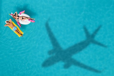 Image of Happy couple with inflatable ring and mattress in swimming pool, top view. Flying airplane casting shadow on water