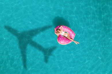 Image of Young happy woman with inflatable ring in swimming pool, top view. Flying airplane casting shadow on water