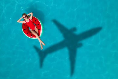 Image of Young happy woman with inflatable ring in swimming pool, top view. Flying airplane casting shadow on water