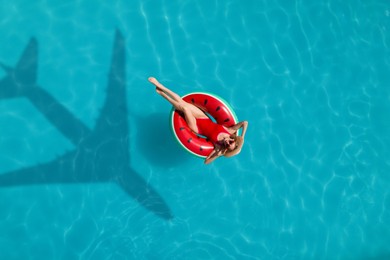 Image of Young happy woman with inflatable ring in swimming pool, top view. Flying airplane casting shadow on water