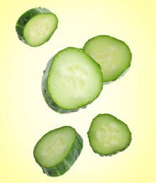 Image of Pieces of fresh cucumbers falling on yellow gradient background