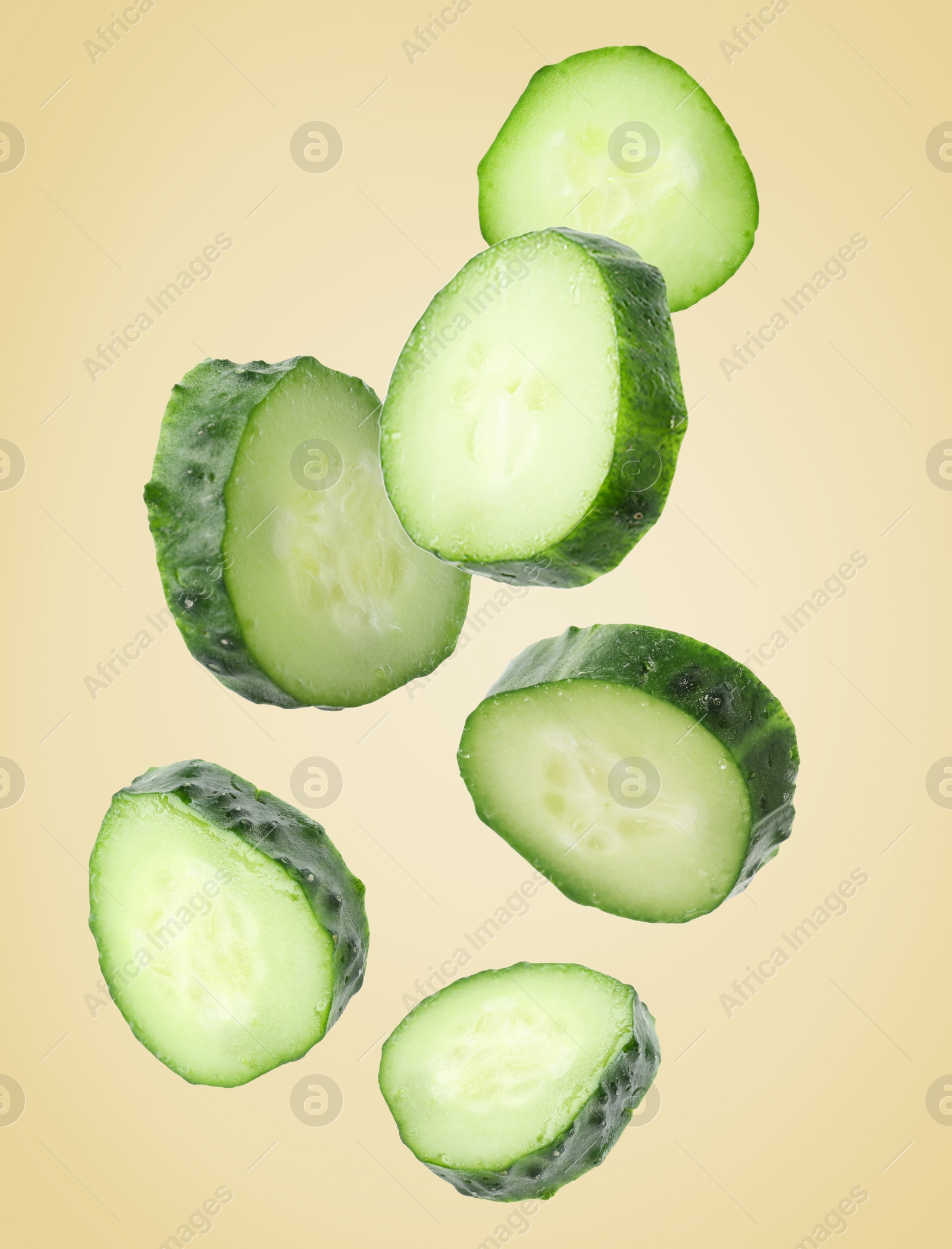 Image of Pieces of fresh cucumbers falling on beige gradient background