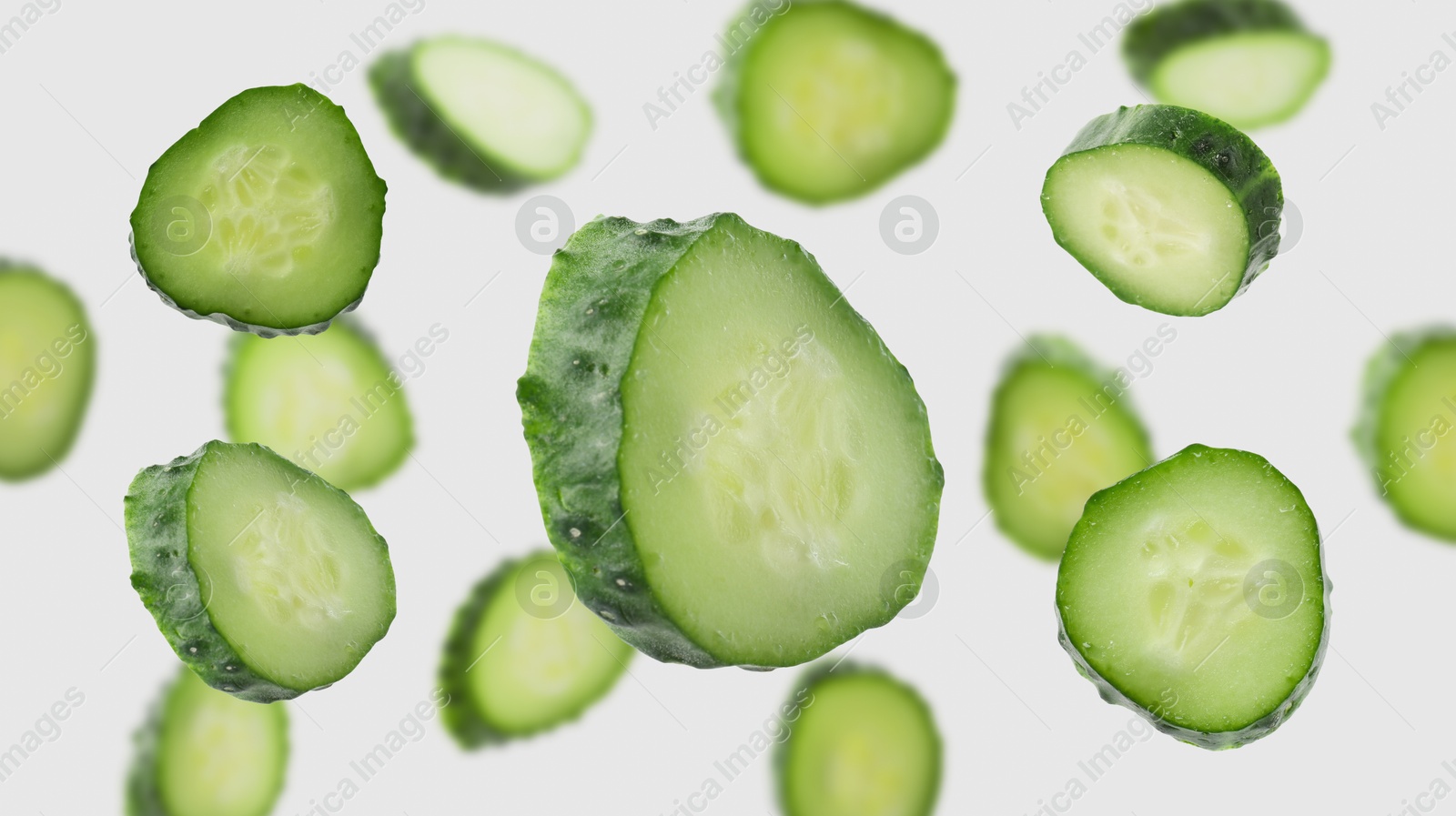 Pieces of fresh cucumbers falling on light background Image of Pieces of fresh cucumbers falling on light background