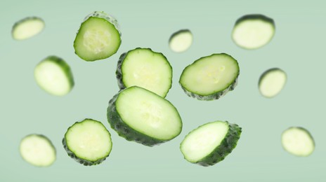 Image of Pieces of fresh cucumbers falling on light green background