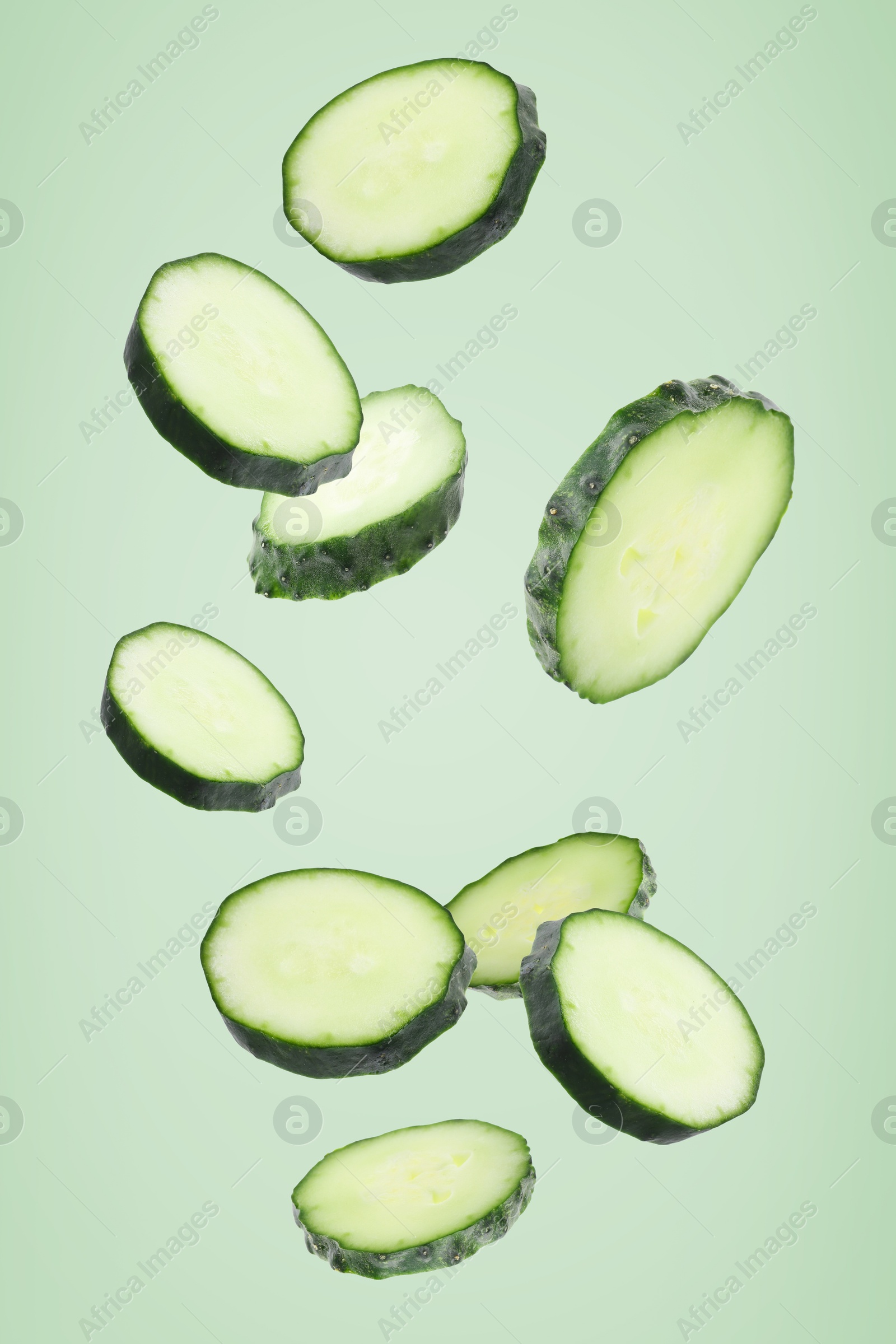Pieces of fresh cucumbers falling on light green background Image of Pieces of fresh cucumbers falling on light green background