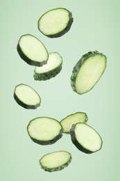 Image of Pieces of fresh cucumbers falling on light green background