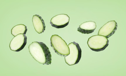 Image of Pieces of fresh cucumbers falling on green background