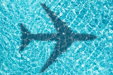 Image of Flying airplane casting shadow on water, top view