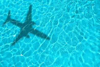 Image of Flying airplane casting shadow on water, top view