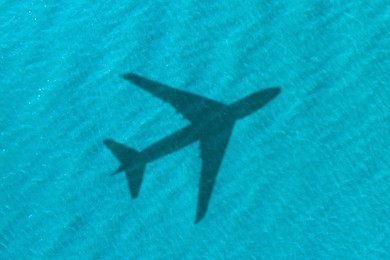 Image of Flying airplane casting shadow on water, top view