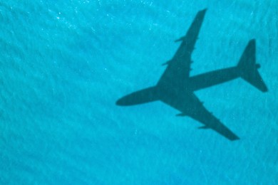 Image of Flying airplane casting shadow on water, top view