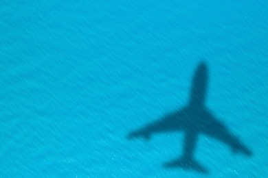 Image of Flying airplane casting shadow on water, top view