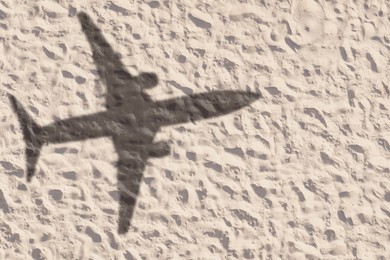 Image of Flying airplane casting shadow on sand, top view