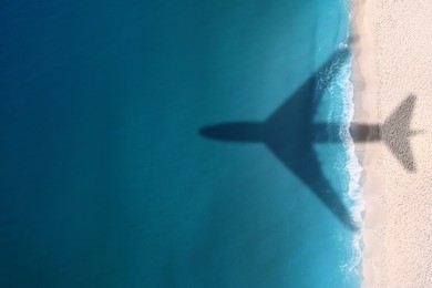 Image of Flying airplane casting shadow on sandy beach and water, top view