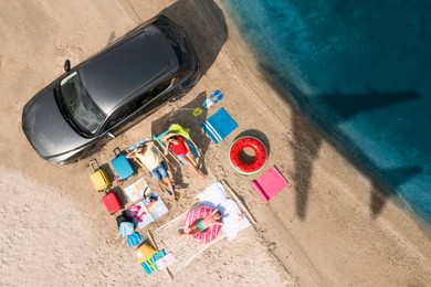 Image of Family with beach accessories and car near sea. Flying airplane casting shadow on sand and water