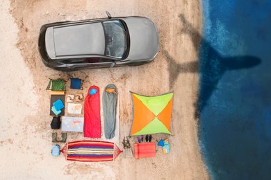 Image of Car and camping equipment on beach. Flying airplane casting shadow on sand and water