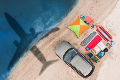 Image of Car and camping equipment on beach. Flying airplane casting shadow on sand and water