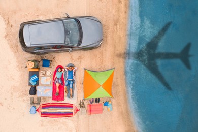 Image of Couple with car and camping equipment on beach. Flying airplane casting shadow on sand and water