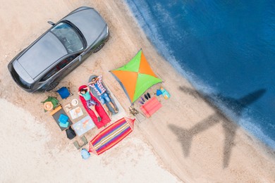 Image of Couple with car and camping equipment on beach. Flying airplane casting shadow on sand and water