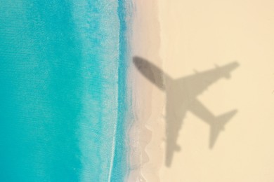Image of Flying airplane casting shadow on sandy beach, top view