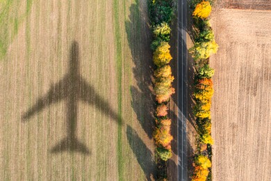 Image of Flying airplane casting shadow on agricultural field, top view