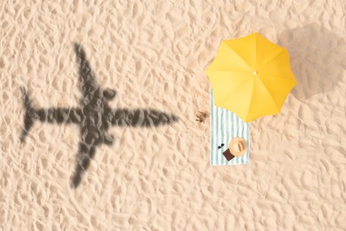 Image of Umbrella and other vacationer's stuff on beach, top view. Flying airplane casting shadow on sand