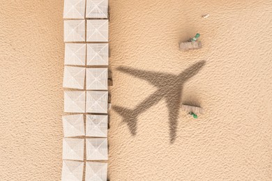 Image of Umbrellas and wooden sunbeds on beach, top view. Flying airplane casting shadow on sand