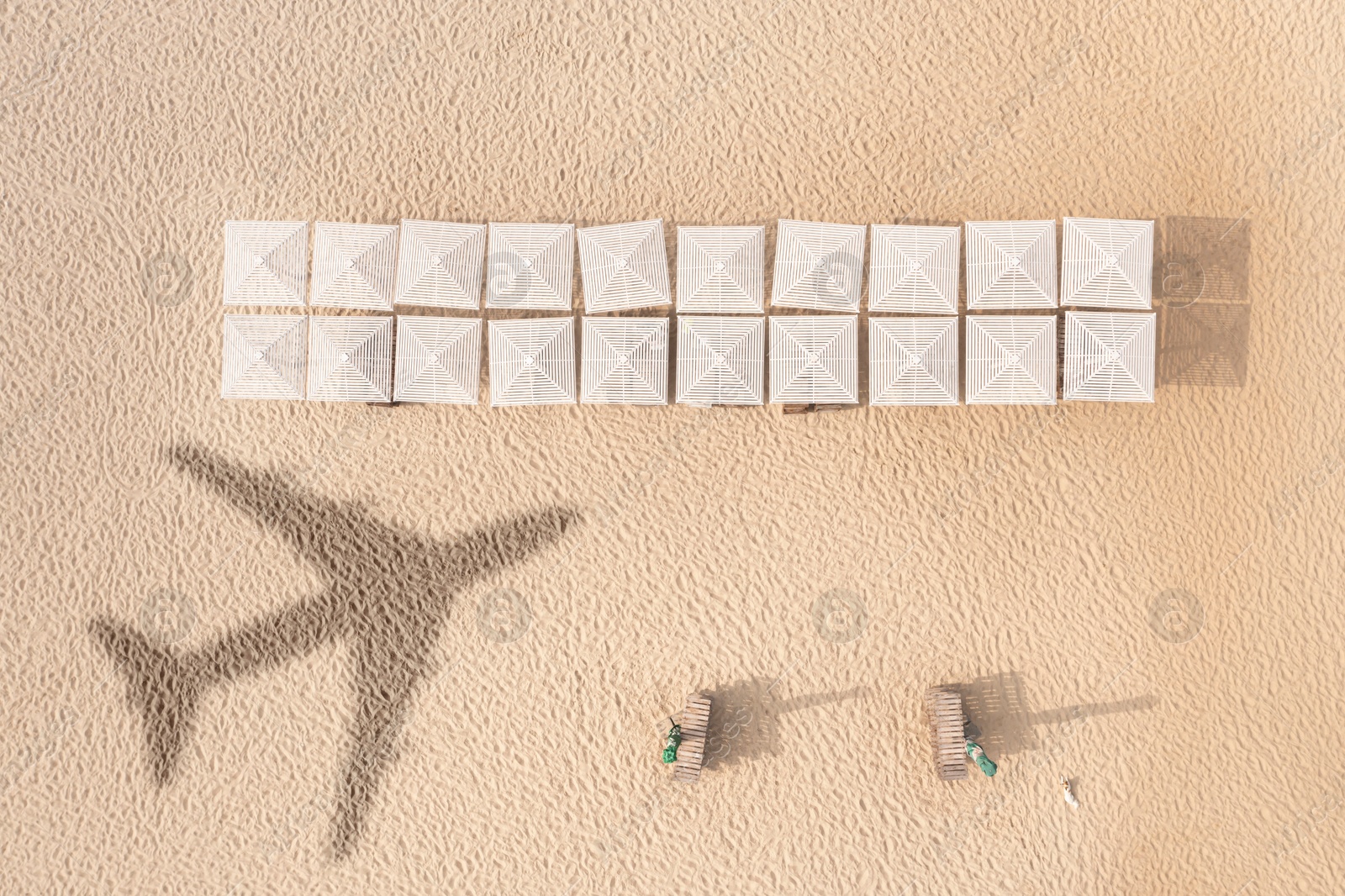 Image of Umbrellas and wooden sunbeds on beach, top view. Flying airplane casting shadow on sand