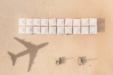 Image of Umbrellas and wooden sunbeds on beach, top view. Flying airplane casting shadow on sand
