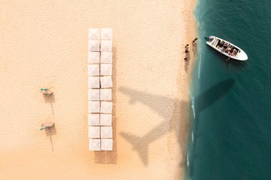 Image of Motorboat near coast with beach umbrellas, top view. Flying airplane casting shadow on sand and water